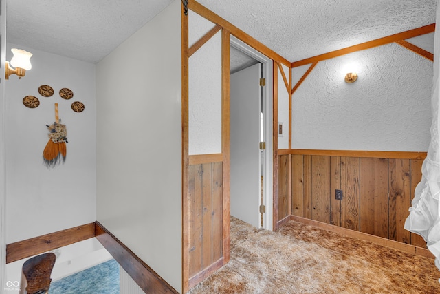 corridor featuring carpet floors, wood walls, a textured ceiling, and a wainscoted wall