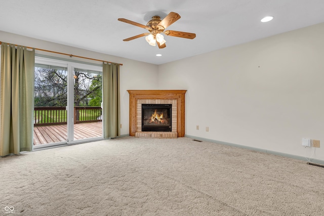 unfurnished living room featuring carpet flooring, a brick fireplace, a ceiling fan, baseboards, and visible vents