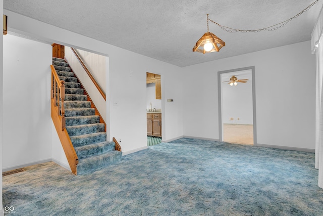 unfurnished living room featuring a ceiling fan, carpet, stairs, and a textured ceiling