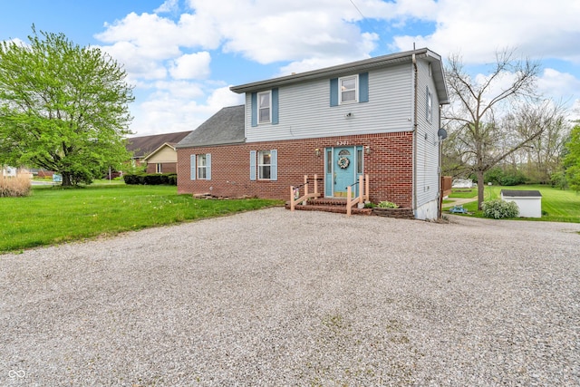 view of front of home featuring brick siding, a front lawn, and gravel driveway