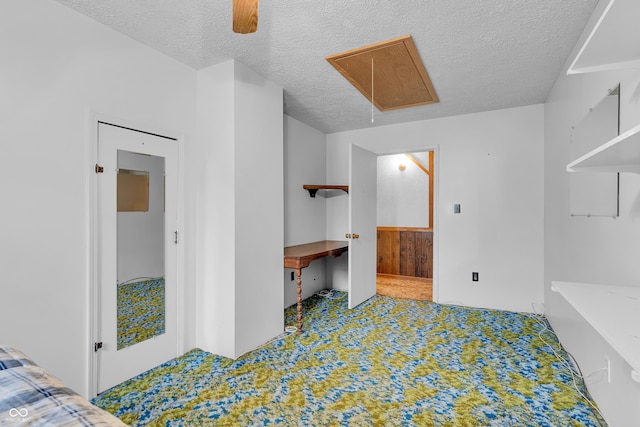 bedroom featuring connected bathroom, ceiling fan, carpet floors, a textured ceiling, and attic access
