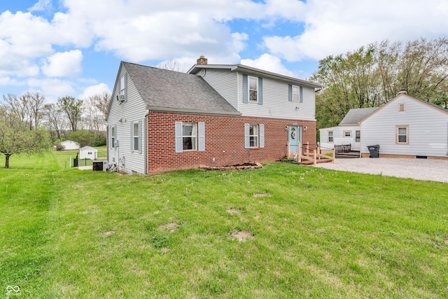 rear view of house with brick siding, a yard, and a chimney