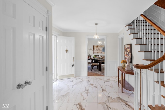 foyer entrance with crown molding, a decorative wall, a wainscoted wall, and stairway