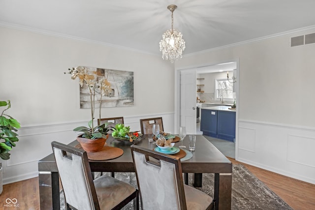 dining room featuring visible vents, a notable chandelier, crown molding, wainscoting, and wood finished floors