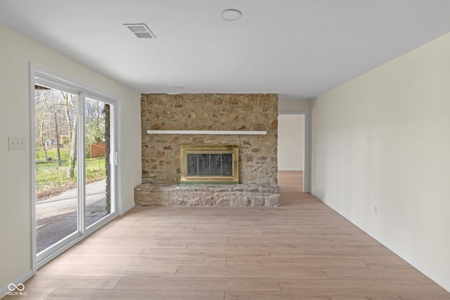 unfurnished living room featuring visible vents, a stone fireplace, and wood finished floors