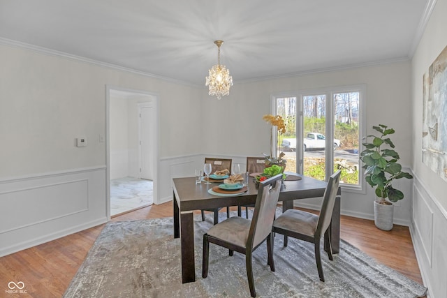 dining space with a wainscoted wall, light wood-type flooring, an inviting chandelier, and ornamental molding