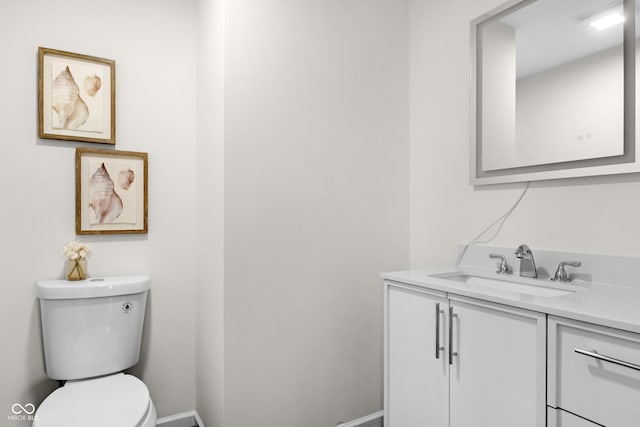 half bathroom with vanity, baseboards, and toilet
