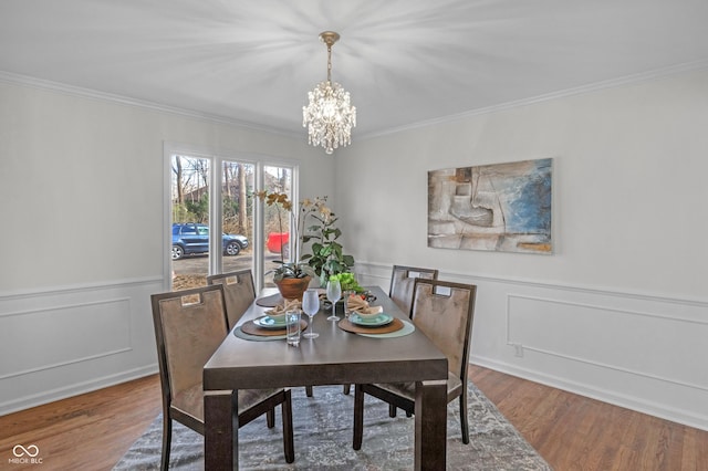 dining room featuring crown molding, a decorative wall, a chandelier, and wood finished floors