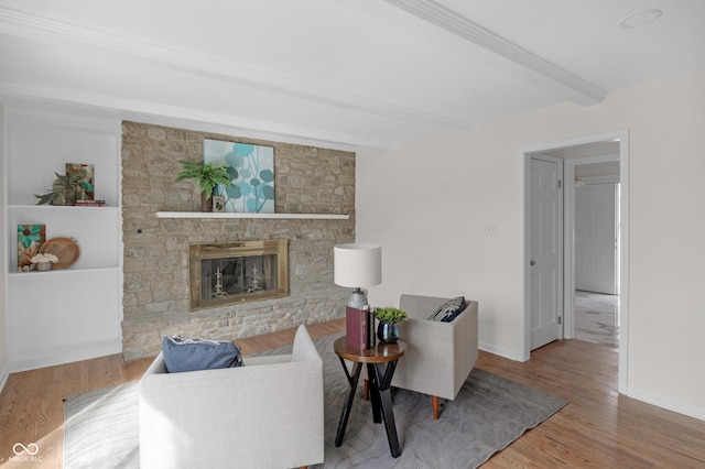 living area featuring a fireplace, baseboards, beamed ceiling, and wood finished floors
