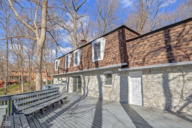 rear view of house featuring mansard roof, a deck, a chimney, and a shingled roof