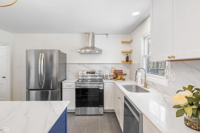 kitchen with tile patterned floors, white cabinets, wall chimney exhaust hood, appliances with stainless steel finishes, and a sink