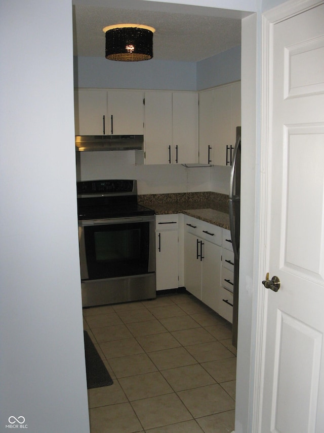 kitchen featuring light tile patterned floors, white cabinetry, dark countertops, stainless steel range with electric stovetop, and under cabinet range hood