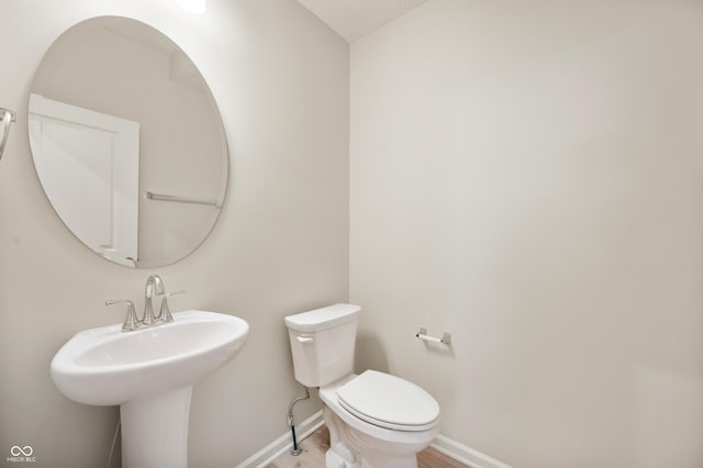 half bathroom featuring baseboards, a sink, toilet, and wood finished floors