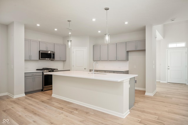kitchen with light wood-type flooring, an island with sink, gray cabinetry, stainless steel appliances, and a sink