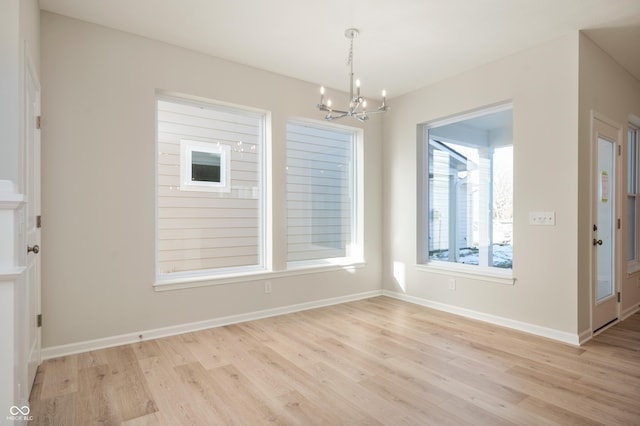 unfurnished dining area with light wood-style flooring, a notable chandelier, and baseboards