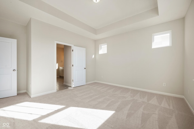 unfurnished bedroom featuring baseboards, a raised ceiling, ensuite bath, and light carpet