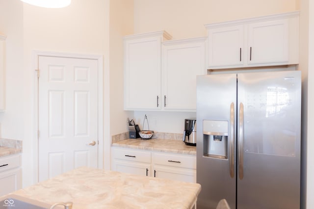 kitchen with white cabinets, light stone counters, and stainless steel fridge