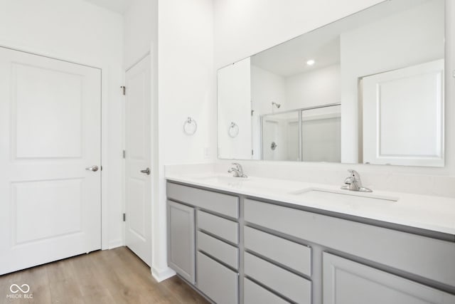 full bath with a shower stall, double vanity, and wood finished floors