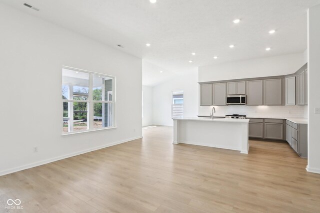 kitchen with gray cabinets, stainless steel microwave, open floor plan, recessed lighting, and backsplash