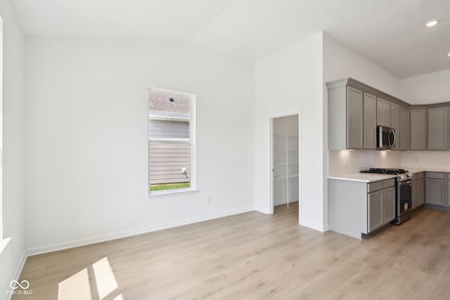 kitchen with appliances with stainless steel finishes, gray cabinetry, backsplash, light wood-style flooring, and light countertops