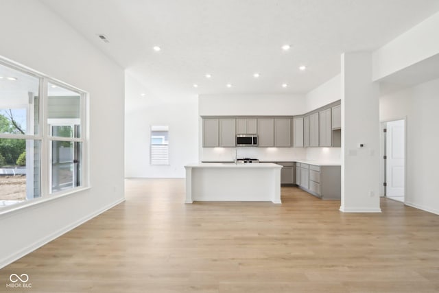 kitchen featuring gray cabinets, stainless steel microwave, healthy amount of natural light, recessed lighting, and a towering ceiling