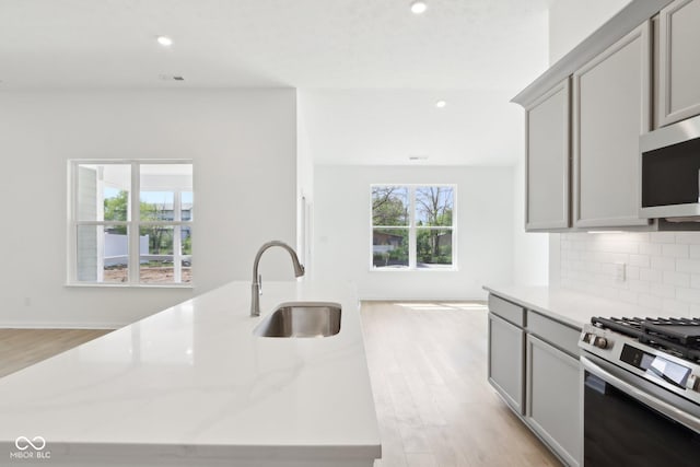kitchen with stainless steel gas range oven, gray cabinets, a sink, light wood-type flooring, and decorative backsplash