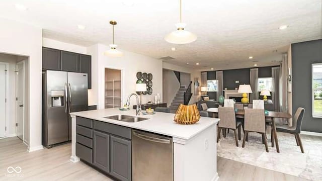kitchen featuring a sink, light countertops, appliances with stainless steel finishes, an island with sink, and light wood finished floors