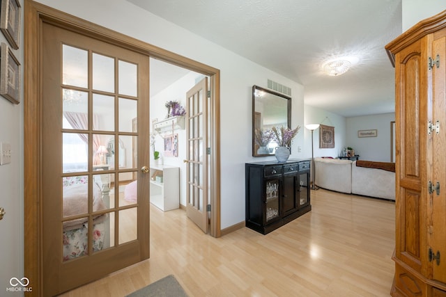 corridor featuring baseboards, visible vents, french doors, and light wood finished floors