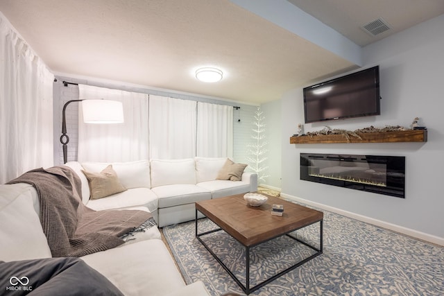 living area featuring a glass covered fireplace, carpet, visible vents, and baseboards