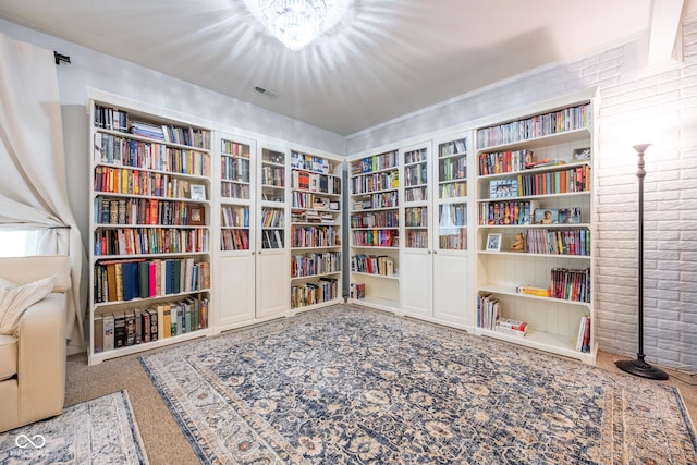 sitting room featuring carpet flooring, visible vents, built in features, brick wall, and bookshelves