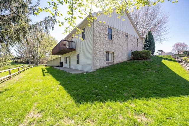 view of property exterior with fence, a wooden deck, brick siding, a patio area, and a yard