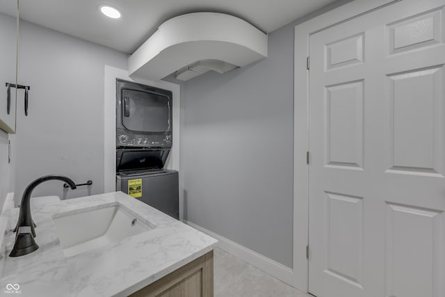 washroom with a sink, baseboards, stacked washing maching and dryer, and laundry area