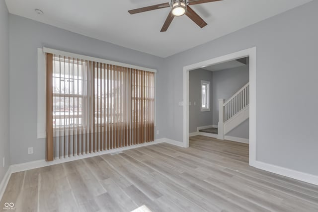 spare room featuring light wood-type flooring, a ceiling fan, baseboards, and stairs
