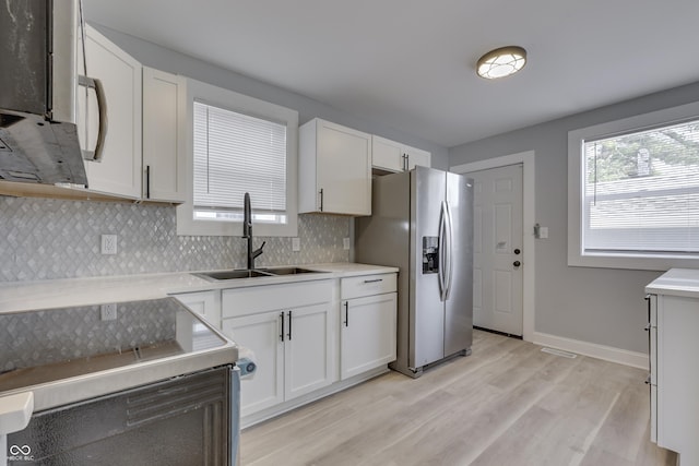 kitchen featuring white cabinets, a sink, stainless steel fridge, range with electric cooktop, and backsplash