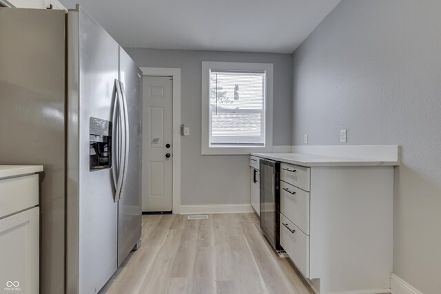 kitchen with baseboards, stainless steel fridge, white cabinetry, light countertops, and light wood finished floors