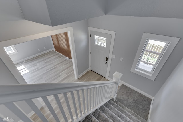 entrance foyer with wood finished floors, baseboards, lofted ceiling, and stairs