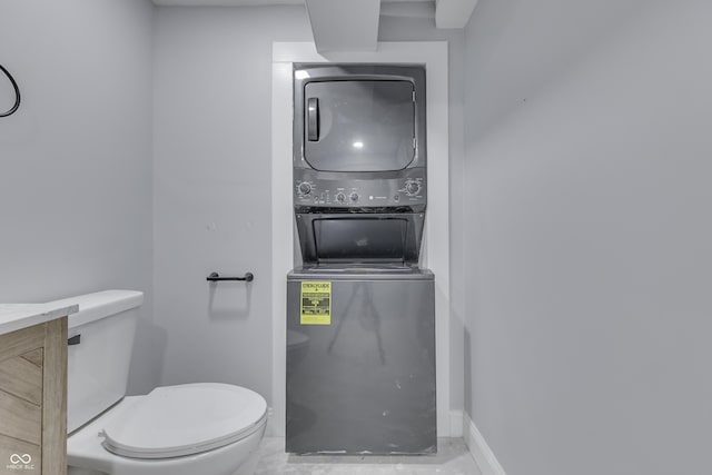 bathroom featuring stacked washer / dryer, vanity, baseboards, and toilet