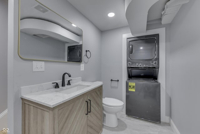 half bath featuring vanity, visible vents, toilet, baseboards, and stacked washer / drying machine