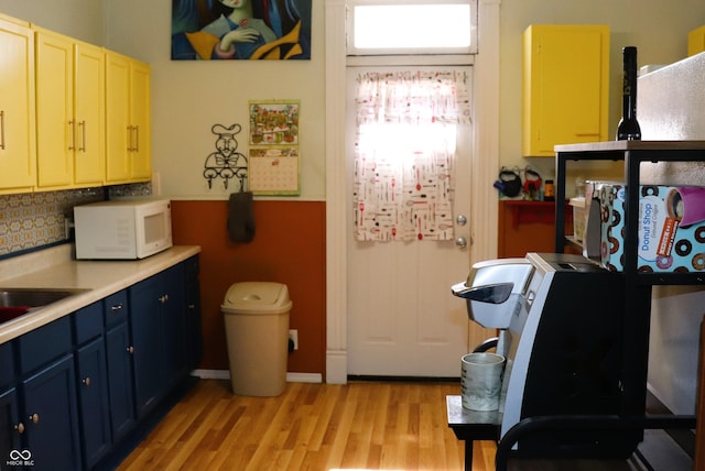 kitchen featuring light countertops, light wood-style floors, white microwave, decorative backsplash, and blue cabinets