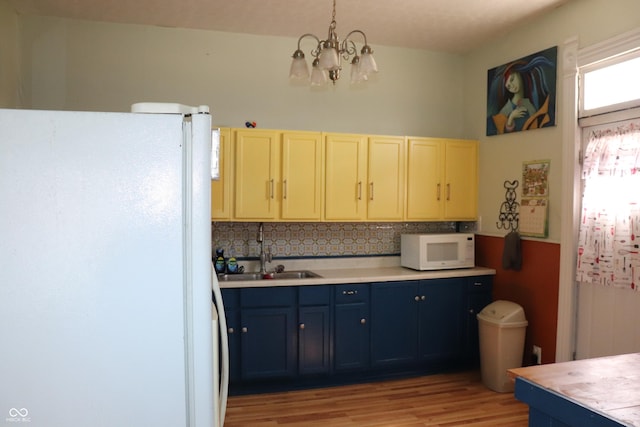 kitchen featuring white appliances, blue cabinetry, light countertops, a sink, and a notable chandelier