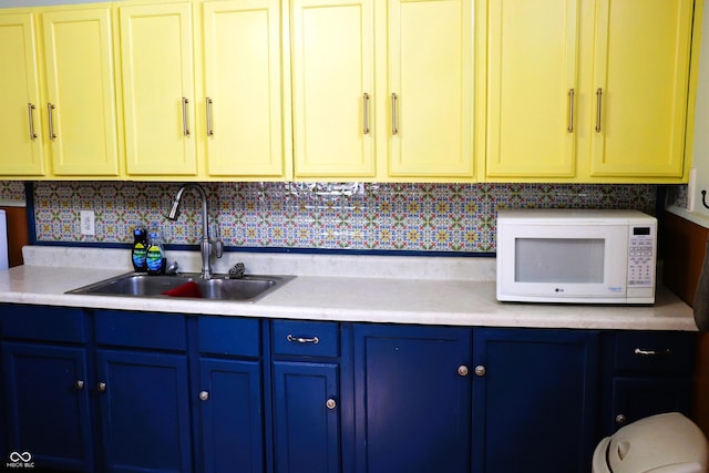 kitchen featuring light countertops, white microwave, a sink, and blue cabinetry