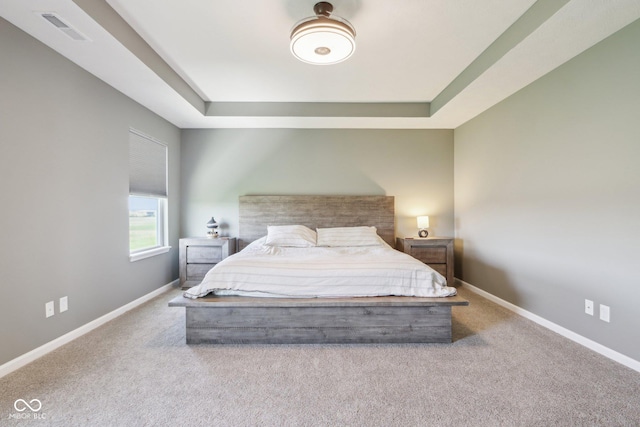 carpeted bedroom featuring visible vents, a tray ceiling, and baseboards