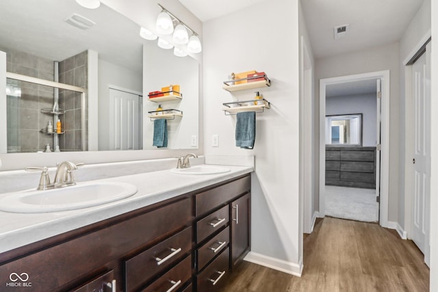 bathroom with double vanity, a sink, a stall shower, and wood finished floors