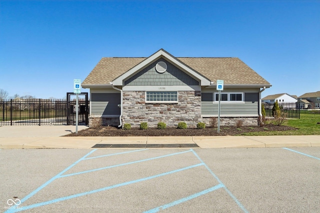 view of front of house with fence, stone siding, and roof with shingles