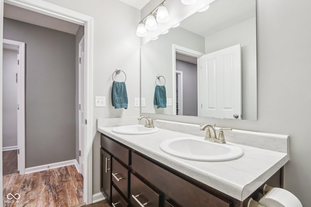 bathroom featuring a sink, baseboards, double vanity, and wood finished floors