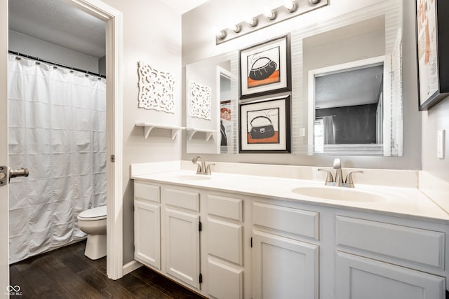 full bath featuring a sink, double vanity, toilet, and wood finished floors