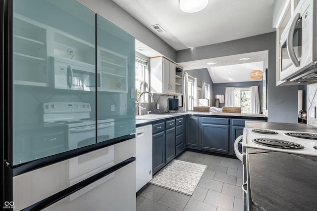 kitchen with blue cabinetry, dark countertops, open shelves, a sink, and white appliances