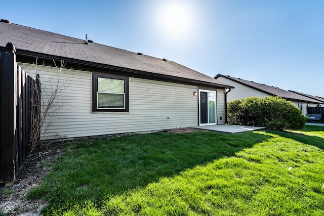 back of property with roof with shingles, a yard, and a patio area