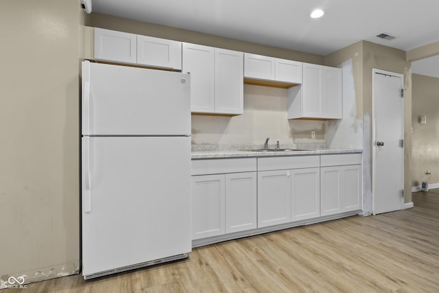 kitchen with freestanding refrigerator, white cabinetry, visible vents, and a sink