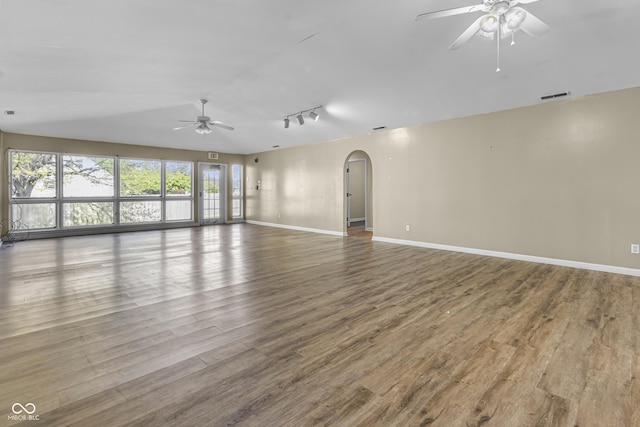 spare room with track lighting, wood finished floors, a ceiling fan, and arched walkways